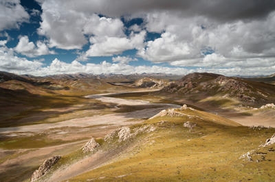 A Chinese valley with stunning hills shadowed by white, puffy clouds